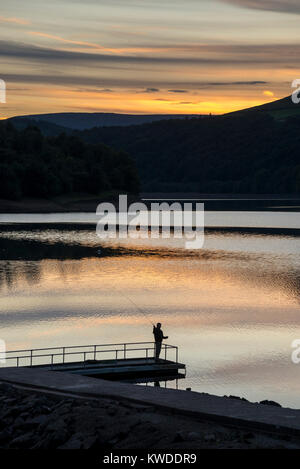 Beau coucher du soleil à Ladybower reservoir dans le Peak District, Derbyshire, Angleterre. Un pêcheur sur la jetée. Banque D'Images