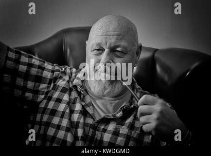 Un mâle adulte assis sur une chaise à droite tenant une pipe, dans une démarche réflexive de l'humeur. Banque D'Images