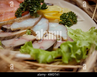 Morceaux de poisson fumé de variétés différentes sont disposés sur une assiette décorée avec des feuilles de salade verte. Banque D'Images