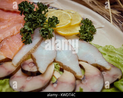 Morceaux de poisson fumé de variétés différentes sont disposés sur une assiette décorée avec des feuilles de salade verte. Banque D'Images