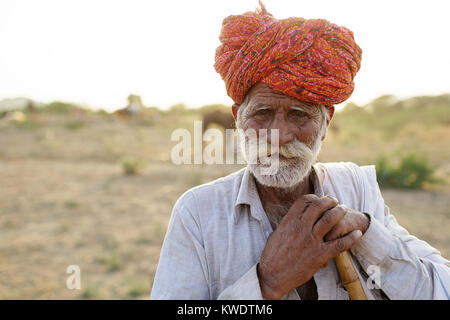 Scène à Pushkar Camel Fair, Portrait of a senior man traderwith moustache wearing red turban penchées sur un bâton, Rajasthan, Inde. Banque D'Images