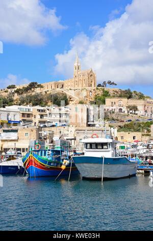 Bateaux de pêche traditionnelle dans le port avec l'église Notre Dame de Lourdes sur la colline à l'arrière, Mgarr, Gozo, Malte, l'Europe. Banque D'Images