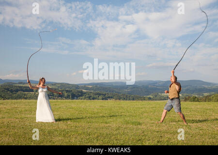 L'homme et la femme avec robe de mariage une journée de formation sur un cheval sur le whip pré herbeux vert sur l'affichage grand paysage en été. Banque D'Images