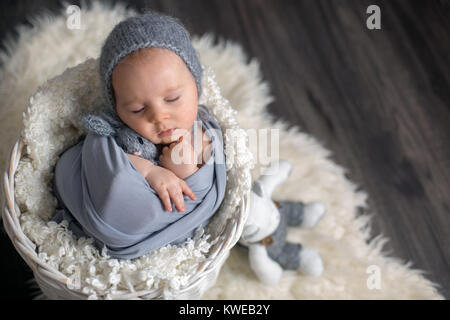 Sweet baby boy in basket, holding et hugging teddy bear, dormir paisiblement enveloppée de foulard gris Banque D'Images