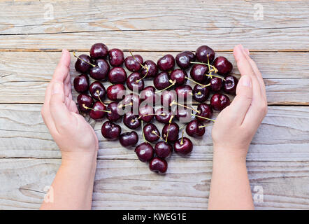 Grand Coeur de cerises mûres et fraîches en prit les mains des femmes sur fond de bois concept de soins de santé et la Saint-valentin journée de la femme Banque D'Images