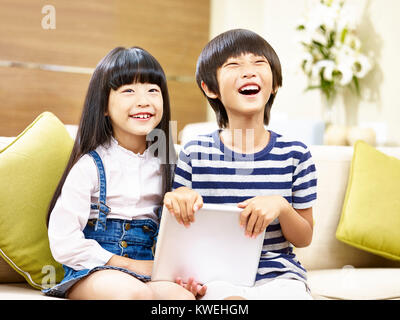 Deux enfants asiatiques mignon petit garçon et petite fille assise sur la table holding digital tablet rire. Banque D'Images