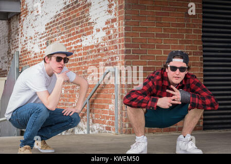 Les jeunes hommes en lunettes de soleil et casquettes snap back posant sur quai de chargement avec mur de brique Banque D'Images