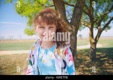 Petite fille dans la nature assis sous un arbre, souriant et regardant la caméra Banque D'Images