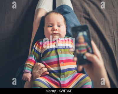 Une mère est en utilisant son smartphone pour prendre une photo de son bébé Banque D'Images