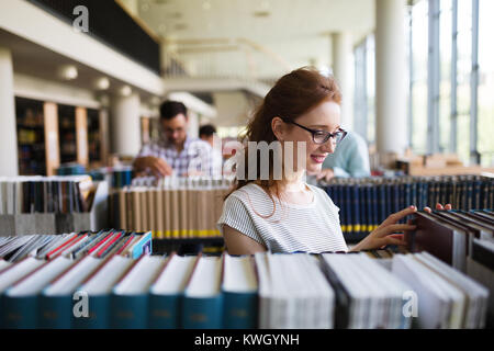 Portrait of a pretty smiling girl reading book in library Banque D'Images