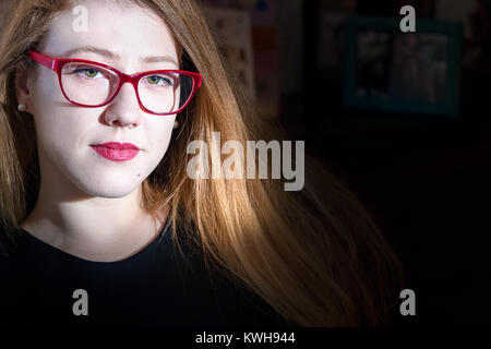 Portrait of a young blonde woman wearing eyeglasses looking at camera, portrait, gros plan d'un éclairage naturel, fond noir, à l'intérieur. Banque D'Images