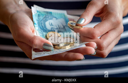 Gros plan des mains d'une femme tenant de l'argent, avec des billets et des pièces de différentes dénominations de la devise du Royaume-Uni . Banque D'Images