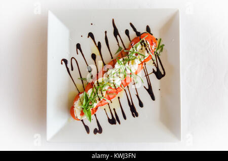 Salade Caprese faite de tranches de mozzarella, tomates et basilic, assaisonné de sel et d'huile d'olive, décoré avec une sauce au chocolat. Banque D'Images