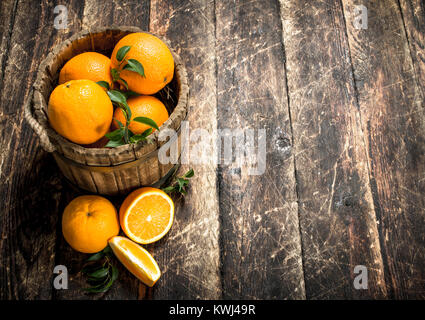 Les oranges fraîches dans un seau en bois. Sur un fond de bois. Banque D'Images