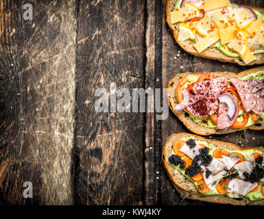 Sandwiches avec des fruits de mer, charcuterie, fromage et légumes. Sur un fond de bois. Banque D'Images