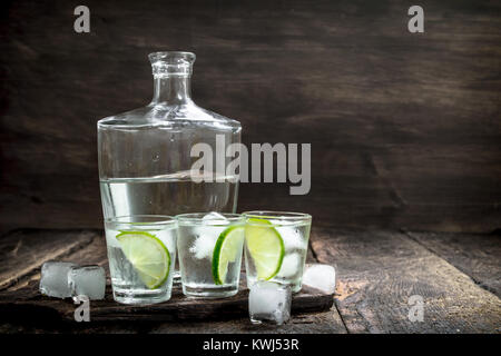 Photos de la vodka avec de la chaux et de la glace sur le bord. Sur un fond de bois. Banque D'Images