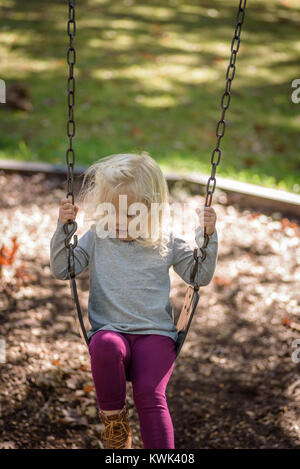 Girl playing on swingset en stationnement sur une journée d'automne ensoleillée Banque D'Images