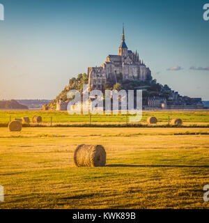 Belle vue sur le Mont Saint-Michel historique célèbre golden dans la lumière du soir au coucher du soleil en été avec des bottes de foin dans les champs, Normandie, France Banque D'Images