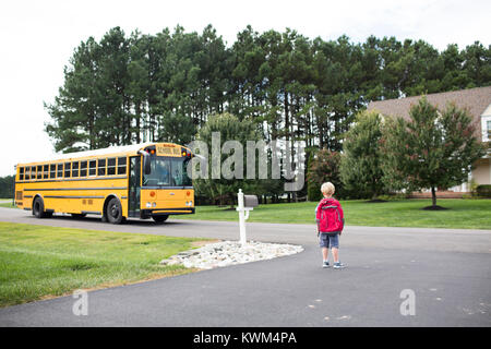 Vue arrière du garçon avec sac à dos en attente pour les autobus scolaires sur route Banque D'Images