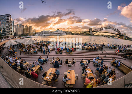 Sydney, Australie - Les touristes et les habitants prendre boissons et happy hour au coucher du soleil sur une chaude soirée d'été près de l'Opéra et le Harbour Bridge. Banque D'Images