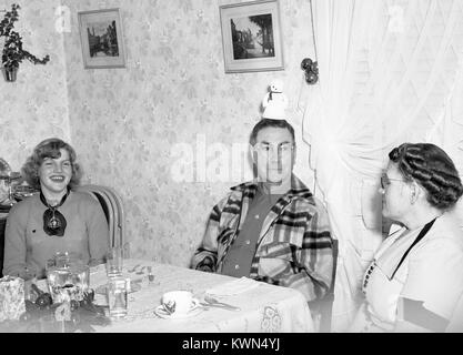 Une famille s'assied à une table de dîner dans une maison de banlieue, le père Goofing autour en plaçant un jouet bonhomme sur sa tête, la fille de rire de son père, de la mère à la recherche d'une expression de désapprobation, Eureka, Californie, 1950. Banque D'Images