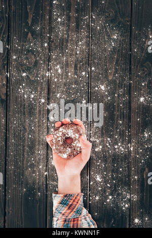 Cropped shot de personne tenant de délicieux donut sur table en bois saupoudrée de farine Banque D'Images