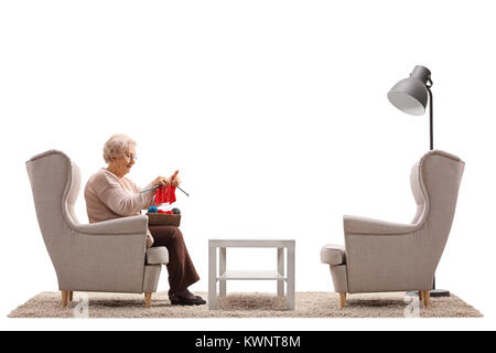 Seule femme âgée assise sur un fauteuil et le tricotage isolé sur fond blanc Banque D'Images