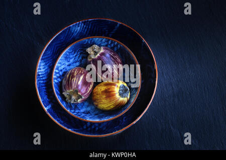 Aubergines violet frais et sains dans un bwols sur pierre sombre arrière-plan. La nourriture végétarienne, la santé ou la cuisine concept, vue de dessus, copy space Banque D'Images