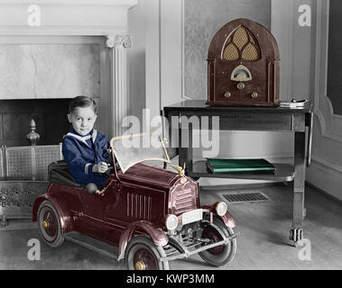 Image vintage d'un jeune garçon dans un costume de marin assis dans une voiture à côté de tuy une vieille radio. Banque D'Images