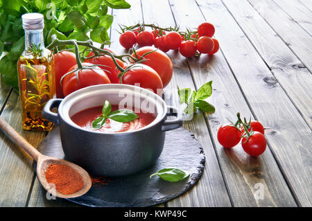 Soupe crème de tomates en céramique noire le moule sur une plaque en pierre servi avec de la crème et le basilic. Ingrédients : tomates, huile végétale et d'épices. Banque D'Images