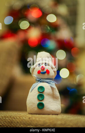 Snowman artisanal fabriqué à partir d'un boudin rempli de riz et décoré avec des boutons avec lumières fond arbre Noël multicolore Banque D'Images