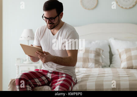 Handsome Young man using digital tablet on bed Banque D'Images