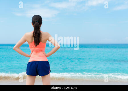 Vue arrière photo de jolie femme élégante formation fini runner standing on beach et relaxant face à belle vue sur l'océan bénéficiant du paysage. Banque D'Images