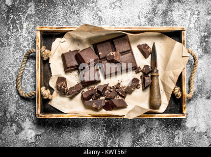 Morceaux de chocolat noir sur un plateau en bois rustique sur un arrière-plan. Banque D'Images