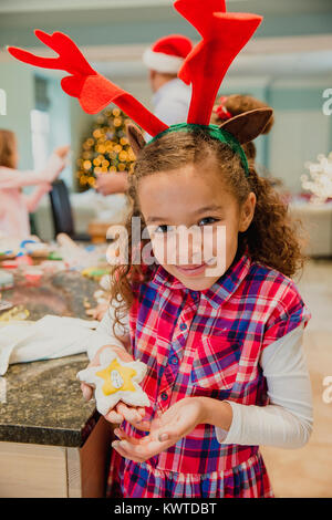 Petite fille est fière posant pour l'appareil photo avec un biscuit de Noël qu'elle a fait avec sa famille à la maison. Banque D'Images