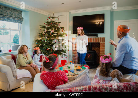 Famille jouent aux charades au moment de Noël dans le salon de leur maison. C'est au tour de la mère et tout le monde essaie de deviner. Banque D'Images