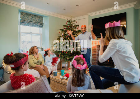 Famille jouent aux charades au moment de Noël dans le salon de leur maison. C'est au tour de la grand-mère et tout le monde essaie de deviner. Banque D'Images