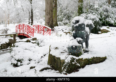 Chien Foo chinois statue de bronze et le pont japonais dans la neige en décembre à Batsford Arboretum, Cotswolds, Moreton-in-Marsh, Gloucestershire, Angleterre Banque D'Images