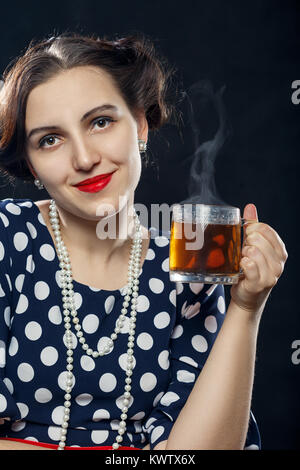 Belle femme pin-up avec une tasse de thé sur fond noir à la caméra en souriant Banque D'Images