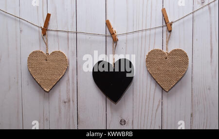 Trois coeurs, l'un noir et deux brunes accrochés sur une ligne en face d'une clôture en bois blanc Banque D'Images
