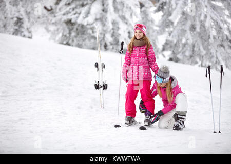 Mère de sa fille met correctement en skis chaussures de ski sur le domaine skiable Banque D'Images