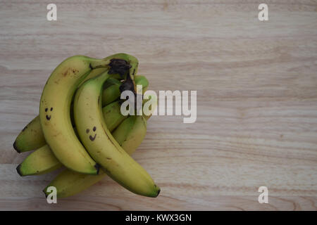 Image de la photographie alimentaire des fruits mûrs de bananes jaunes dans une bande dessinée avec le sourire sur un fond en bois Banque D'Images