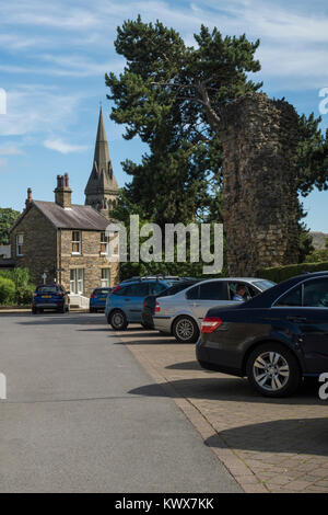 Voitures garées dans le parking du centre-ville en ruines de château aux beaux jours de l'été, avec grand clocher d'église au-delà - Knaresborough, North Yorkshire, Angleterre, Royaume-Uni. Banque D'Images