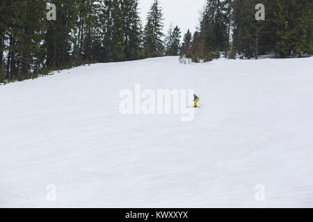 La pente de la montagne est couverte de neige. Le long de celui-ci les arbres pousser. Un skieur est en bas de la pente de ski. Banque D'Images