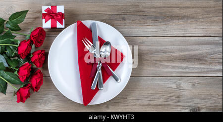 Le dîner de la Saint-Valentin avec une demi-douzaine de roses rouges et de l'argenterie sur bois rustique en vue mise à plat Banque D'Images