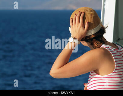 Jeune femme touristiques voyager en bateau sur la mer Egée, en Grèce, au cours des vacances d'été, attraper son chapeau de paille à cause du vent et regarder la mer Banque D'Images