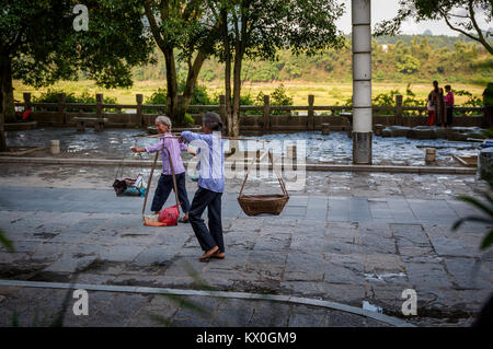 Yangshuo, Chine - 1 août 2012 : Deux chinois femme transportant des produits agricoles sur les poteaux de l'épaule dans une rue de la ville de Yangshuo en Chine, Asi Banque D'Images