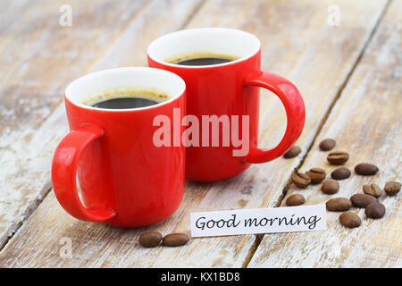 Bonjour carte avec deux tasses de café rouge et les grains de café sur surface rustique Banque D'Images