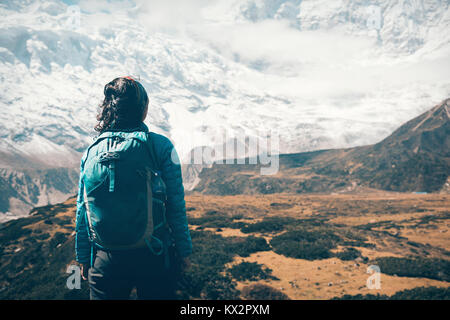 Femme debout avec sac à dos à la recherche sur de belles montagnes couvertes de neige dans les nuages au coucher du soleil. Paysage avec girl, de hautes roches avec des sommets enneigés, jaune Banque D'Images
