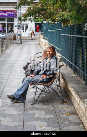 Vers le bas et l'extérieur typique pauvre homme assis sur un banc en bordure de la mendicité de passants à Bucarest, capitale de la Roumanie, de l'Europe centrale Banque D'Images